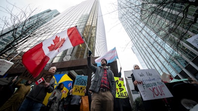 People wave flags and hold signs during a protest outside of the U.S embassy in Vancouver, British Columbia, Tuesday, March 4, 2025.