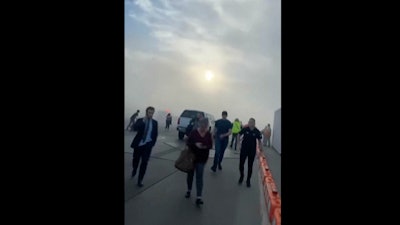 In this image taken from video provided by Justus Rainey, passengers move away from a plane as smoke surrounded the aircraft, in Denver, Thursday, March 13, 2025.