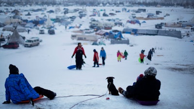 In this Thursday Dec. 1, 2016 file photo, the Oceti Sakowin camp where people have gathered to protest the Dakota Access oil pipeline stands in the background as a children sled down a hill in Cannon Ball, N.D.