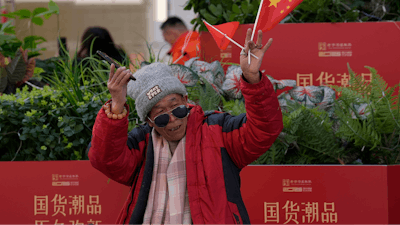 A man waves the Chinese national flag and Communist Party flag in the popular Wangfujing shopping street in Beijing, China, Thursday, March 6, 2025.